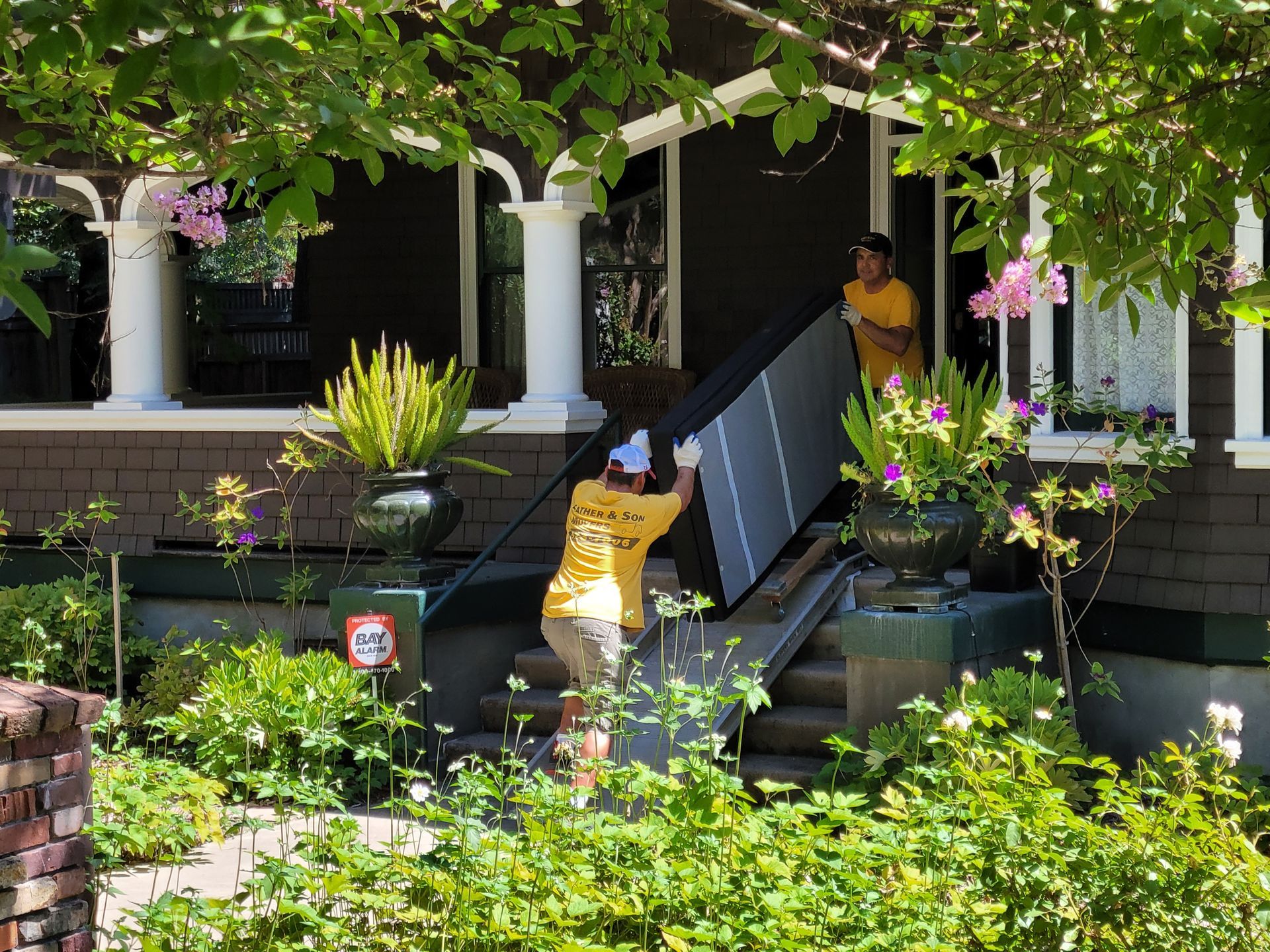 Person carrying a large black object up front steps of a leafy house porch