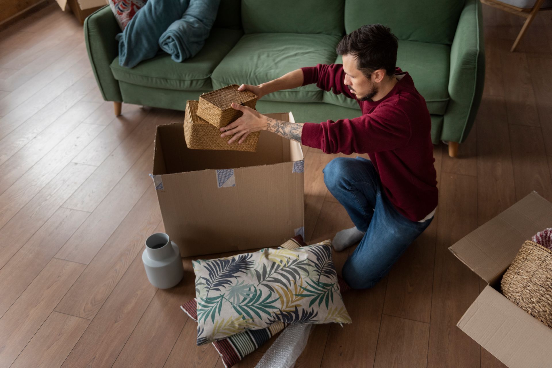 Man packing boxes near a green couch. He's putting a small wooden box in a cardboard box.