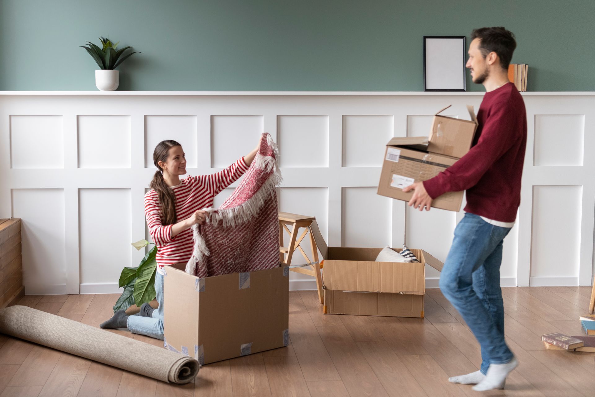 Couple unpacking boxes in a new home, woman placing a rug in a box, man holding boxes.