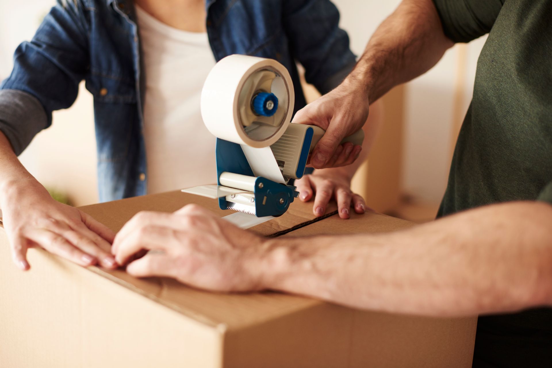 Two people sealing a cardboard box with tape.