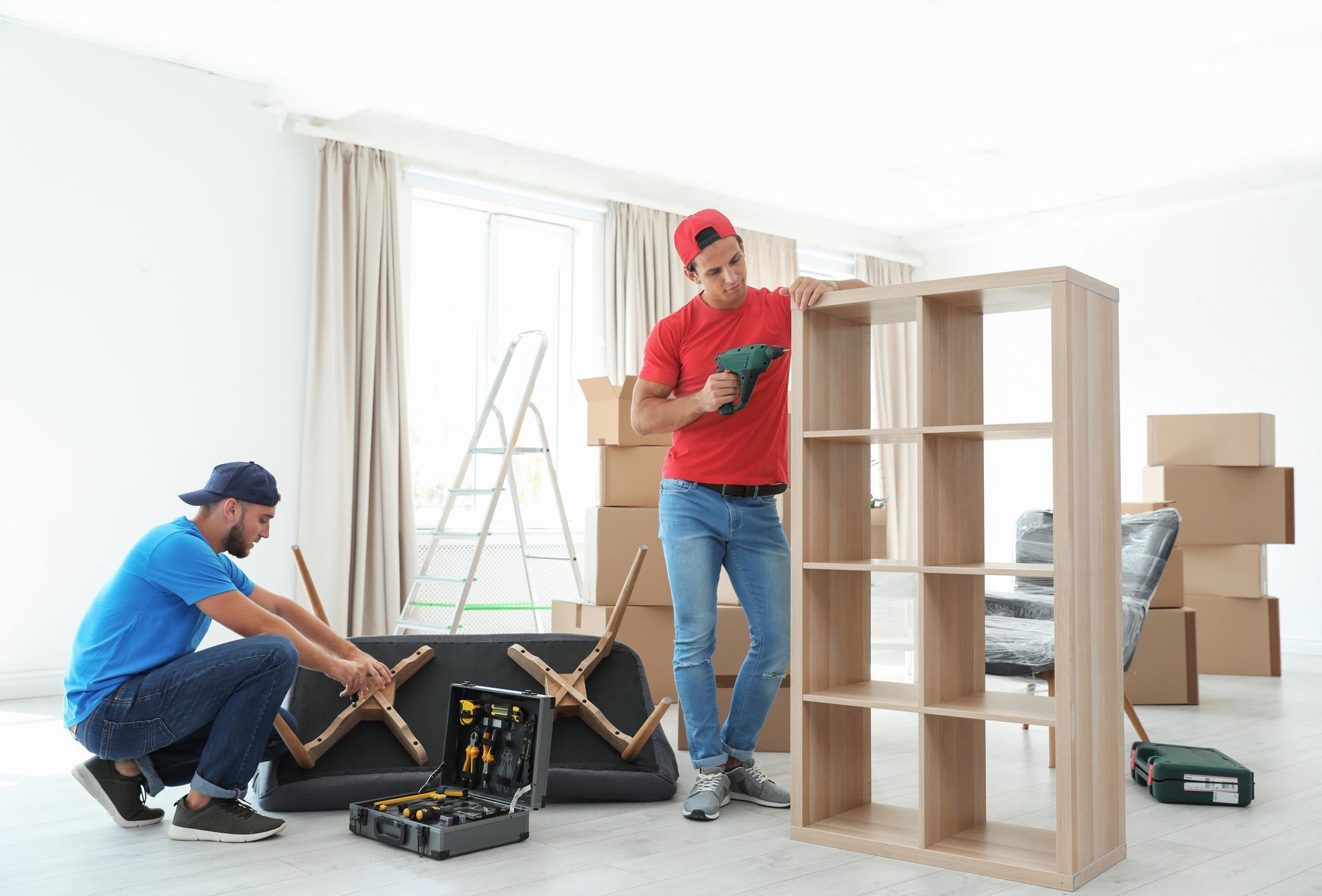 Two men are working on a shelf in a living room.