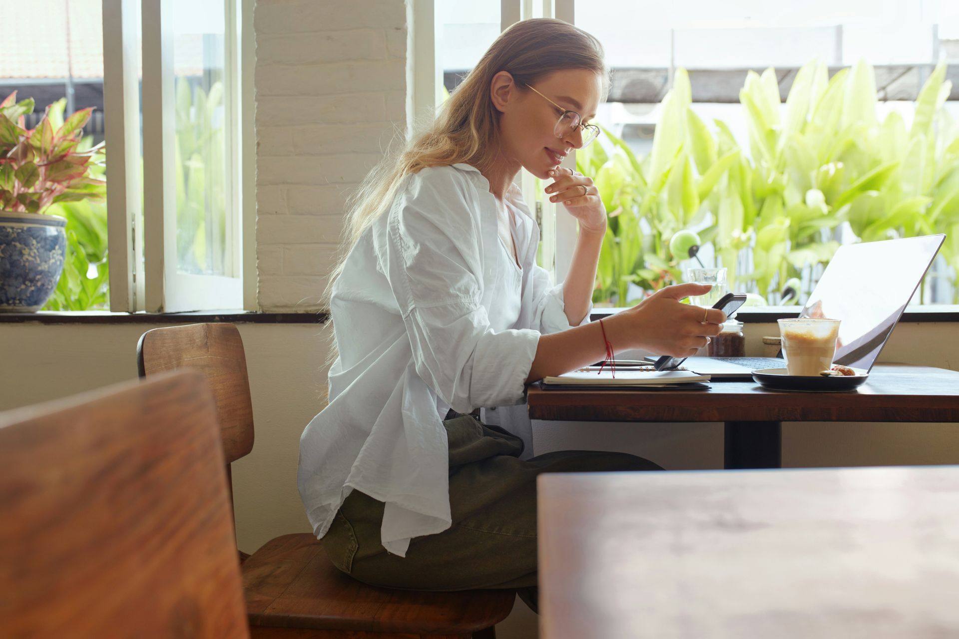 Person in a white shirt working on a laptop at a table in a bright café