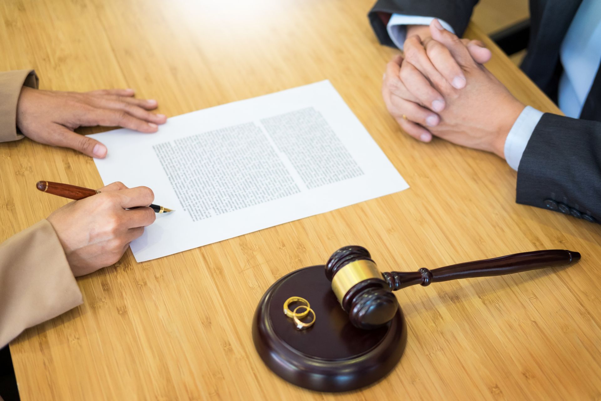 A man and a woman are sitting at a table with a judge 's gavel and wedding rings.