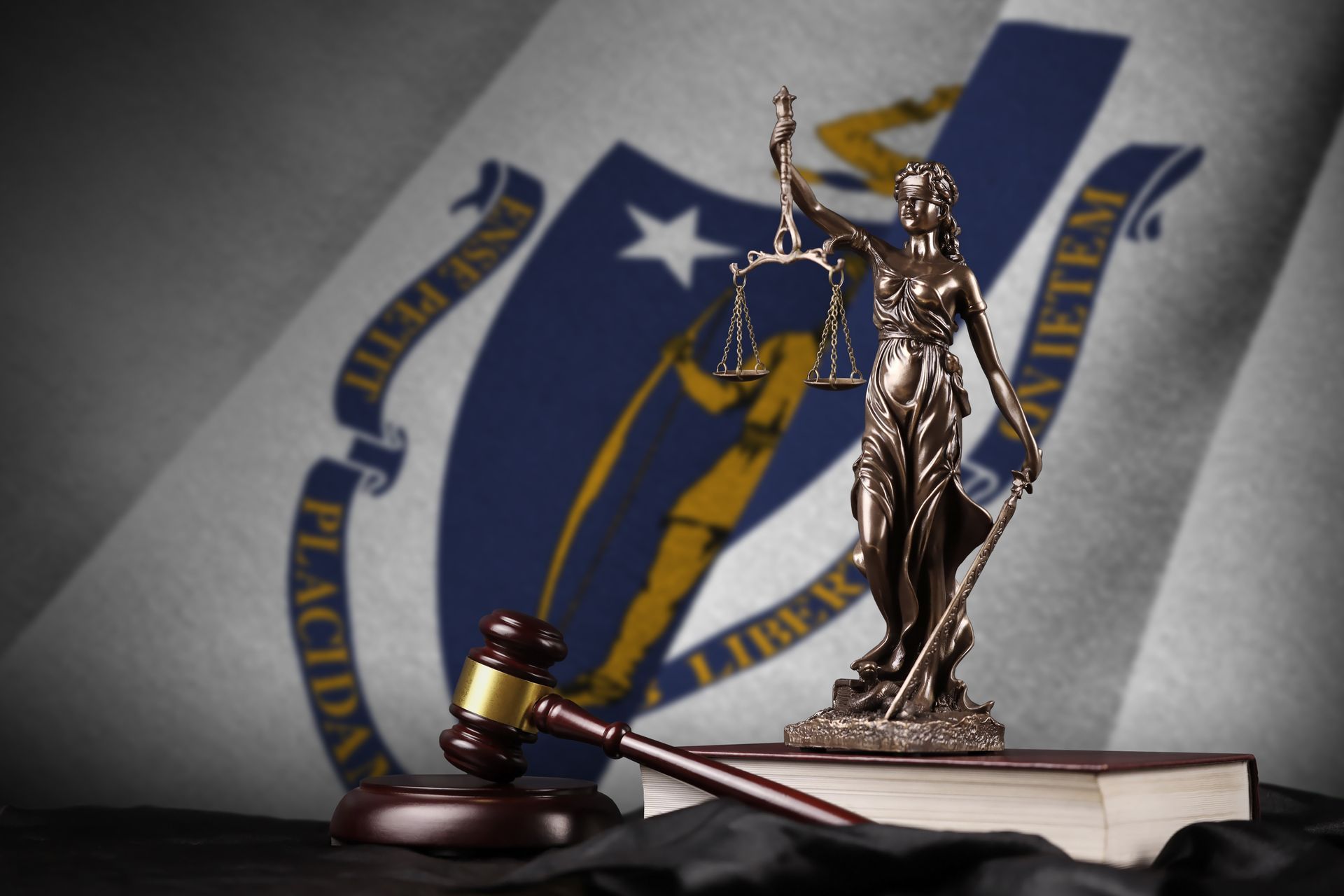 A statue of lady justice sits on top of a book in front of a new hampshire flag