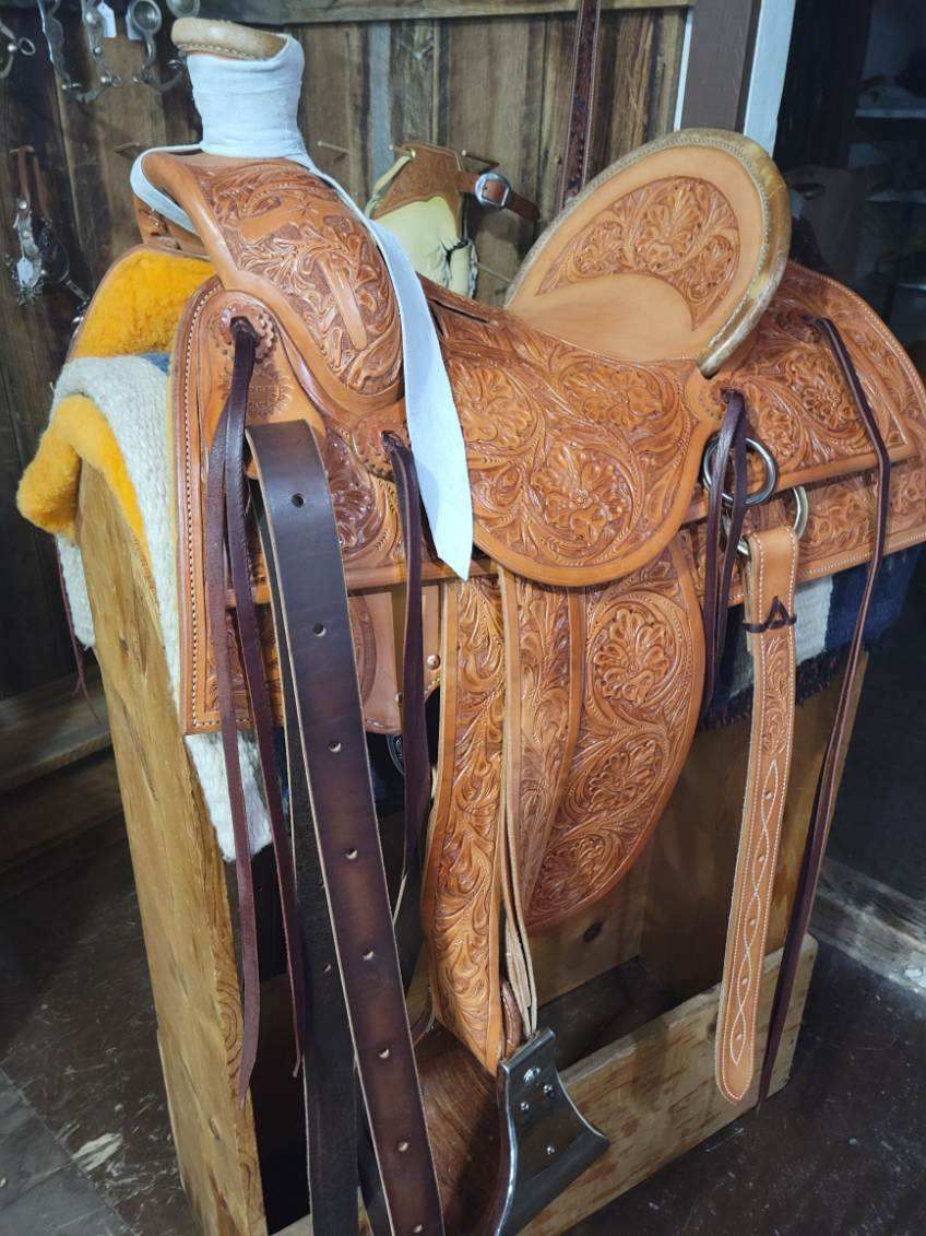 Western saddle and bridles stored on a wooden rack with a tan saddle pad in the background