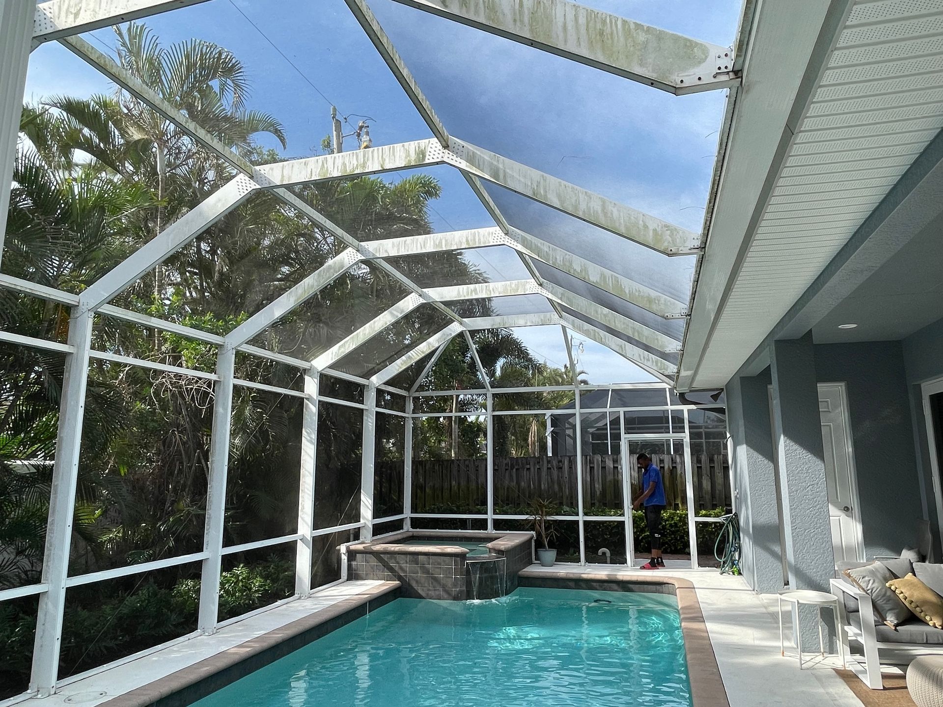 A swimming pool and hot tub enclosed in a white aluminum screen cage next to a house patio on a sunny day.