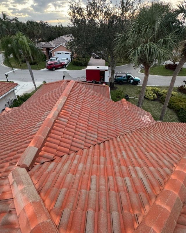 High-angle view of a red terracotta tile roof overlooking a suburban street with parked vehicles and palm trees.
