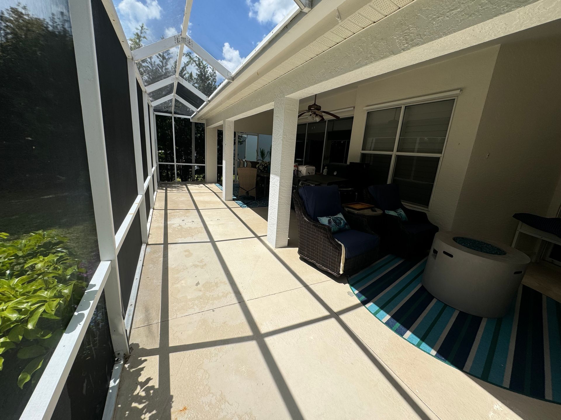 A screened-in patio with concrete flooring, a blue-striped rug, chairs, and a fire pit table under a roof.