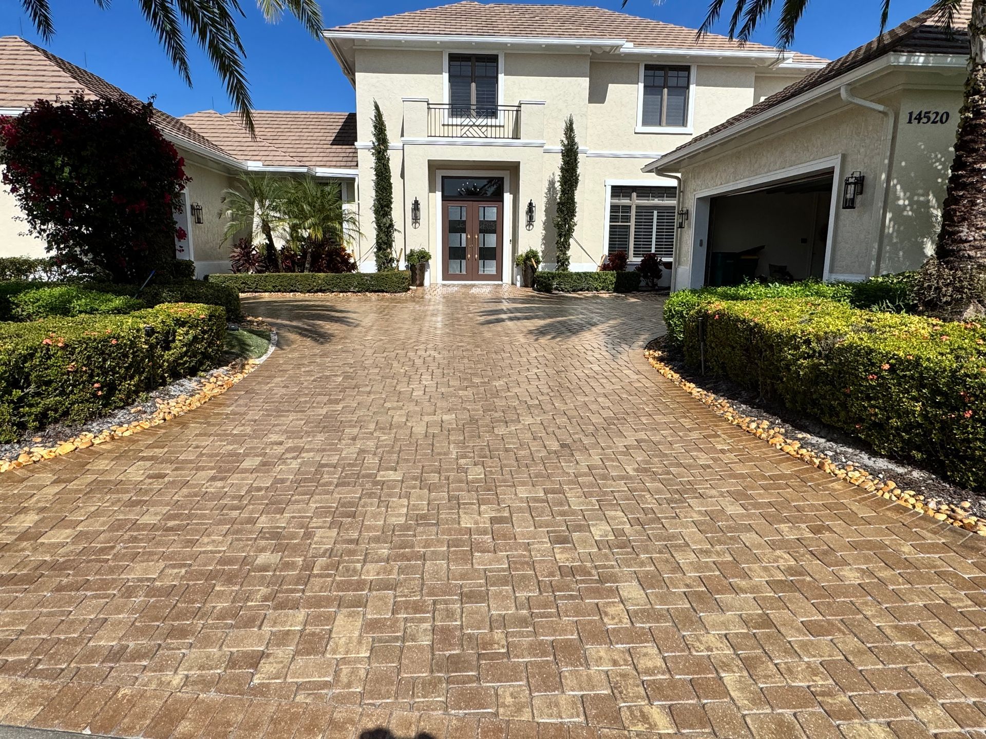 A beige two-story house featuring a large paver driveway leading to a central front entrance and an attached garage.