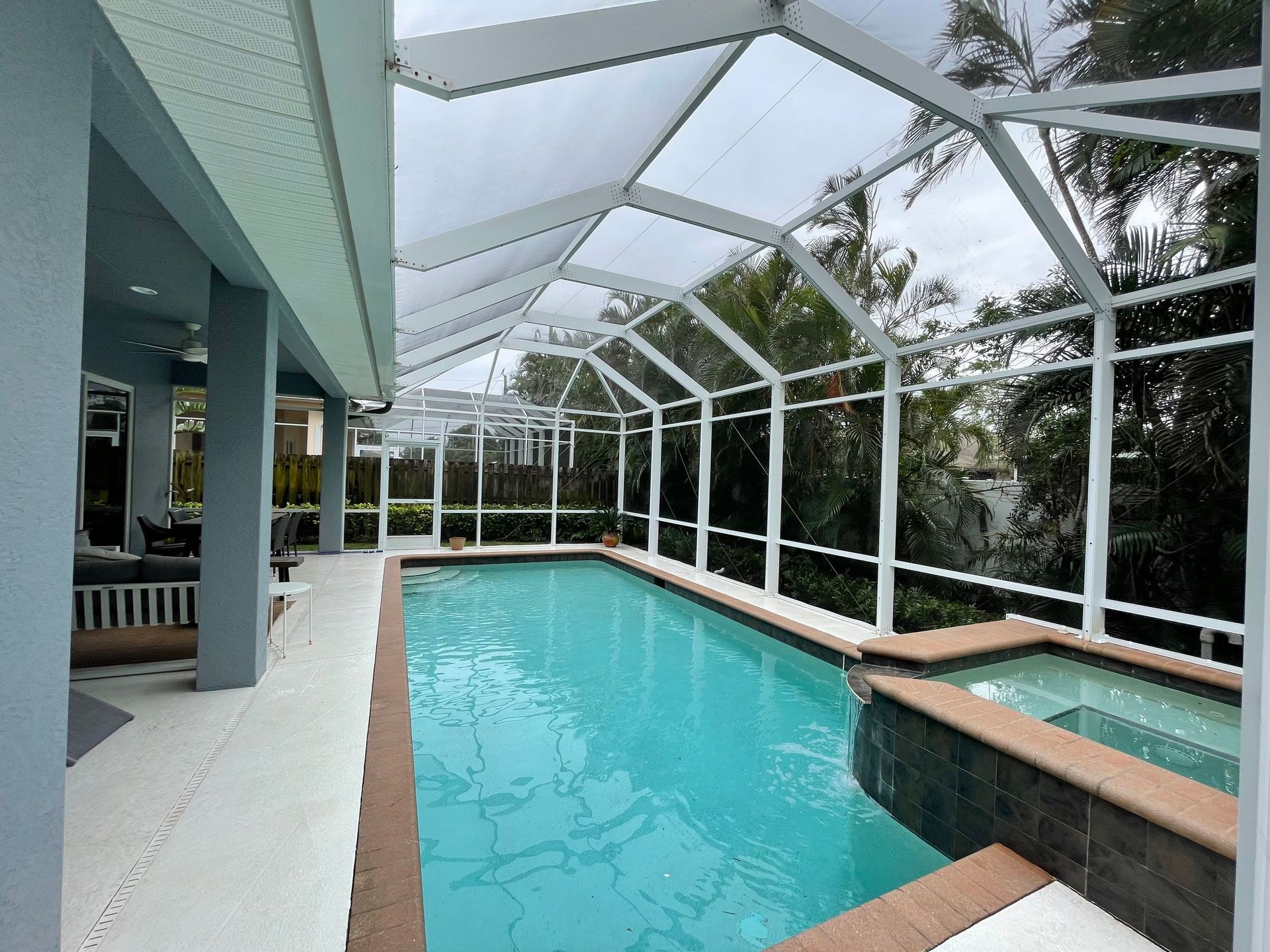 A swimming pool and hot tub enclosed within a white aluminum screened-in patio area next to a blue house exterior.