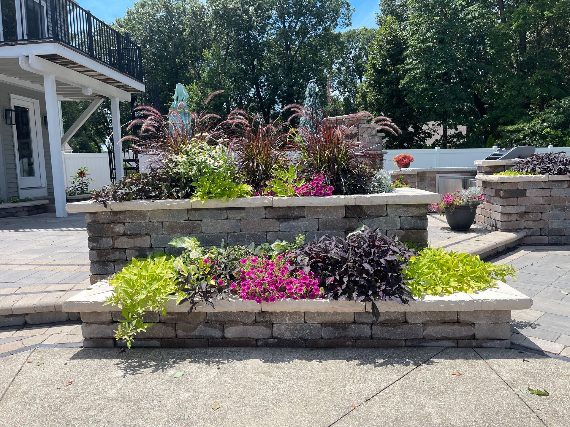 A brick planter filled with flowers and plants in front of a house.