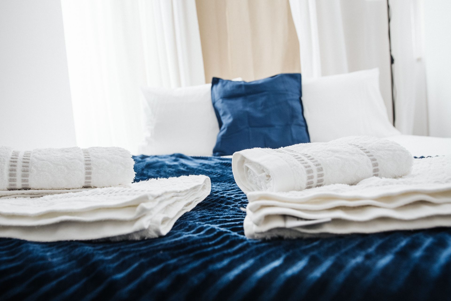 Neatly made bed with blue bedding, white pillows, and folded white towels in a bright room