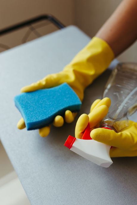 Gloved hands cleaning a surface with sponge and spray bottle on a table