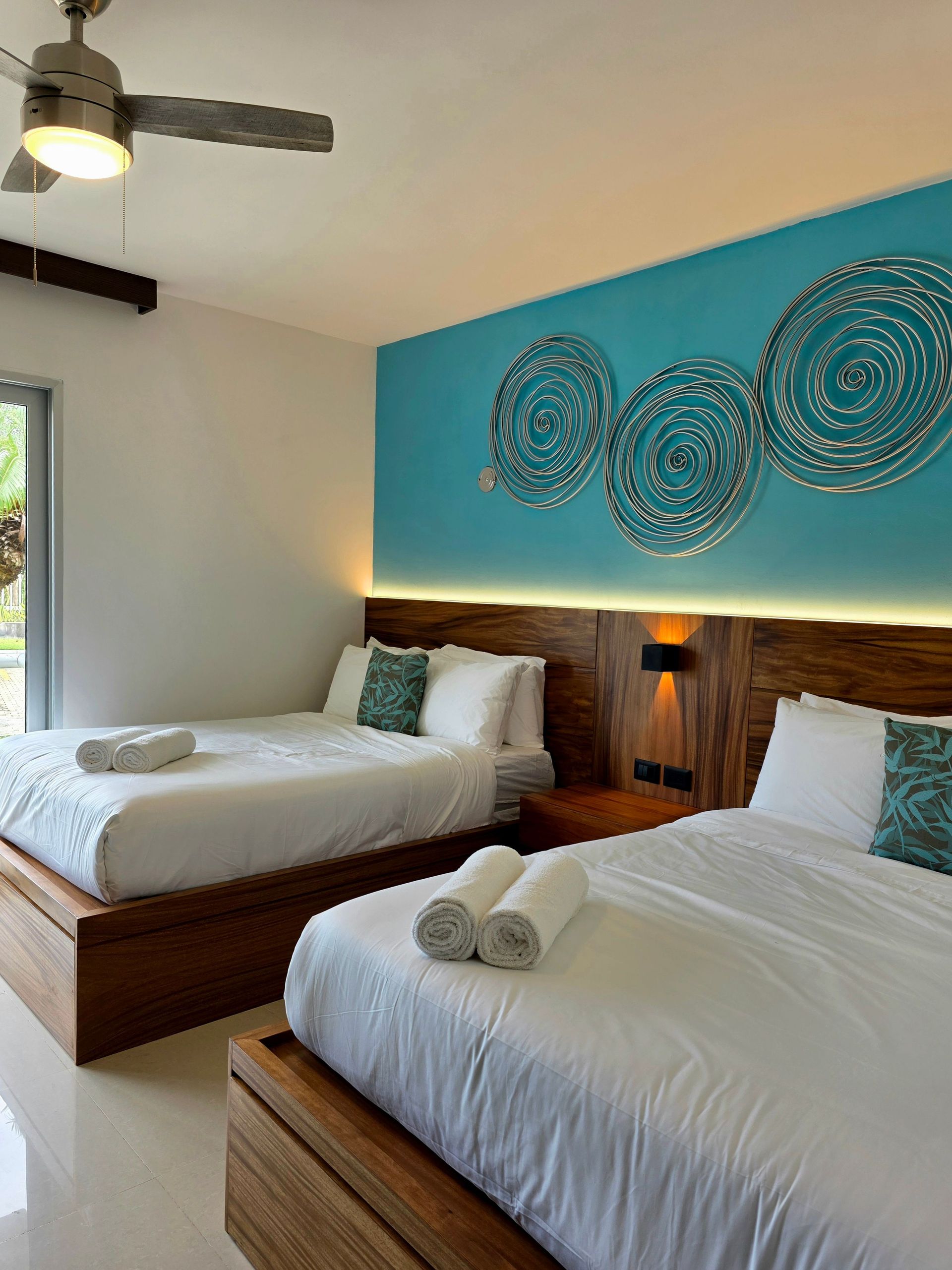 Bright bedroom with two wooden beds, teal accent wall, and decorative wall art
