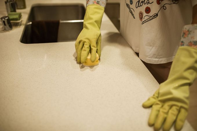 Person in yellow gloves cleaning a kitchen countertop near a sink