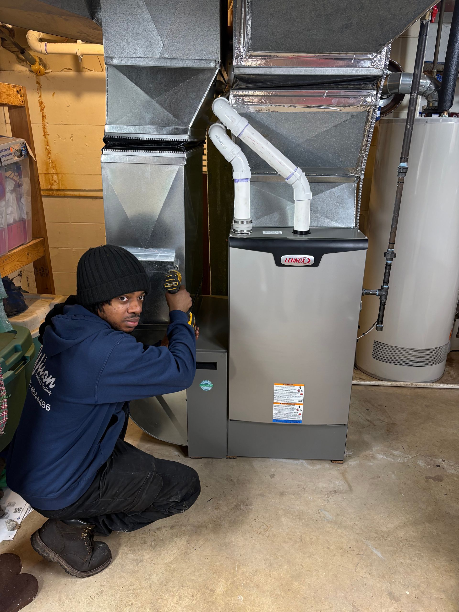 Heat pump unit next to a brick wall and a concrete walkway, with a grassy yard and hedges in the background.