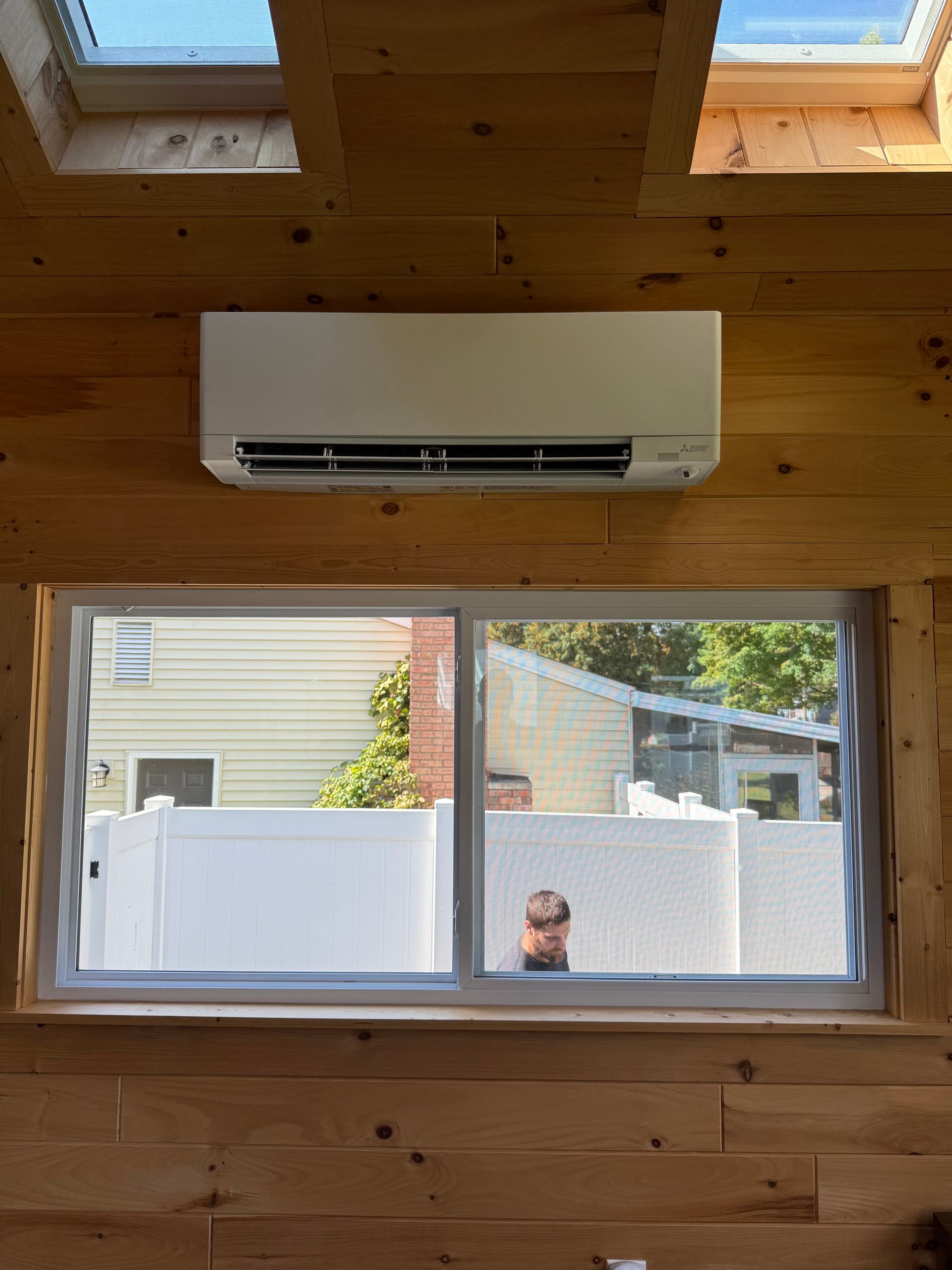 Two air conditioning units near a brick wall, partially shaded by green foliage.