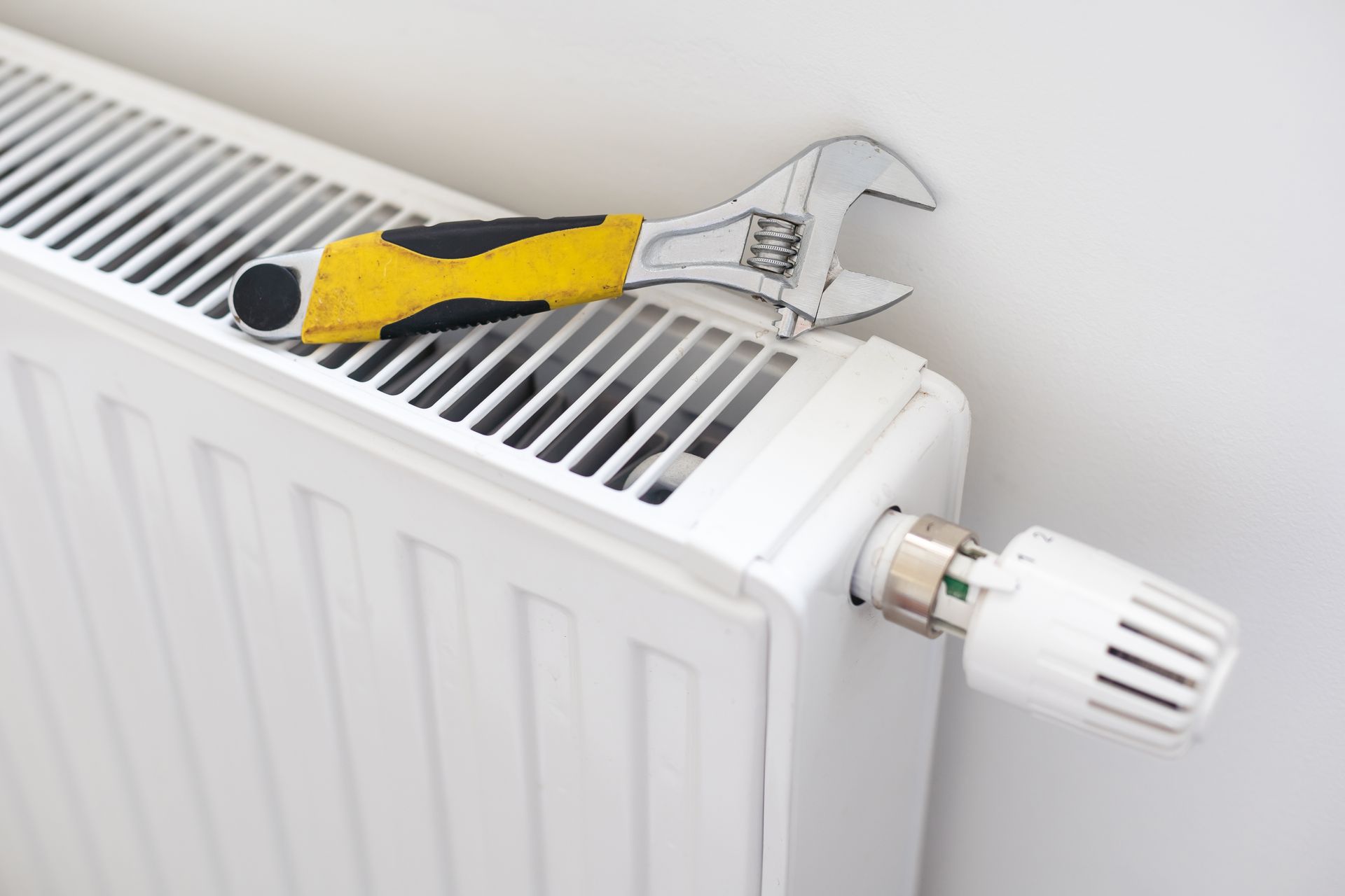 White radiator with an adjustable wrench on top and a white thermostat valve.