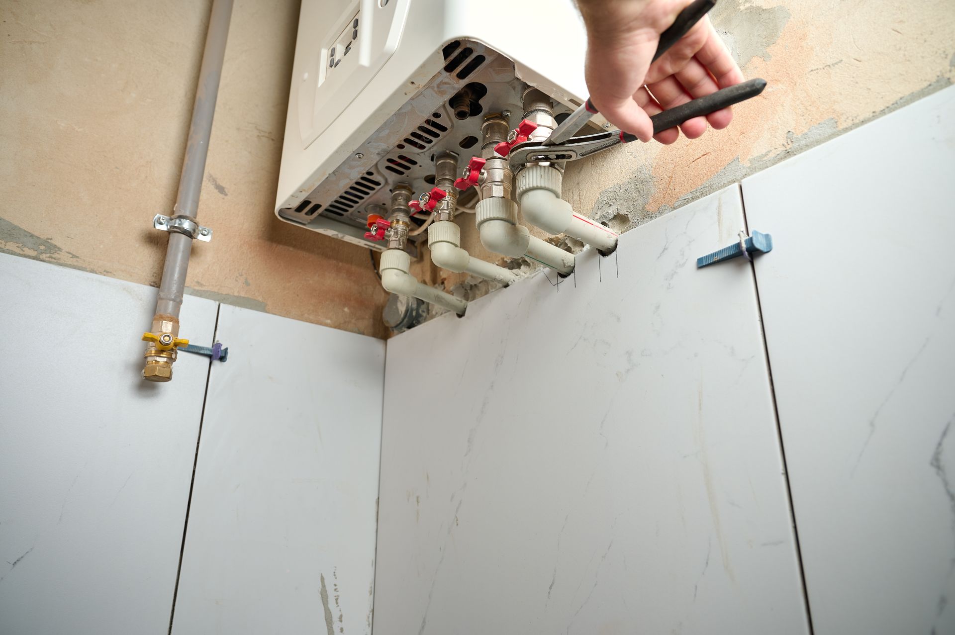 Plumber working on a water heater, attaching pipes in a tiled room.