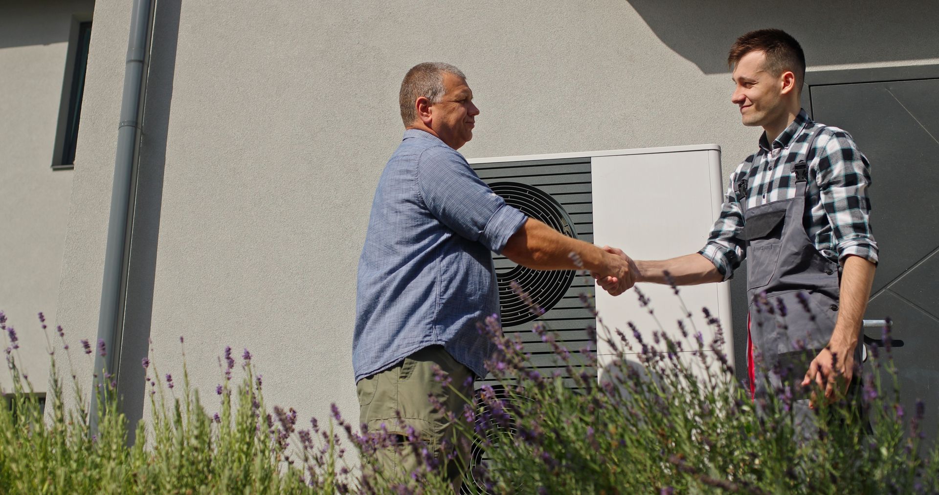Man shaking hands with technician near a building's outdoor unit.