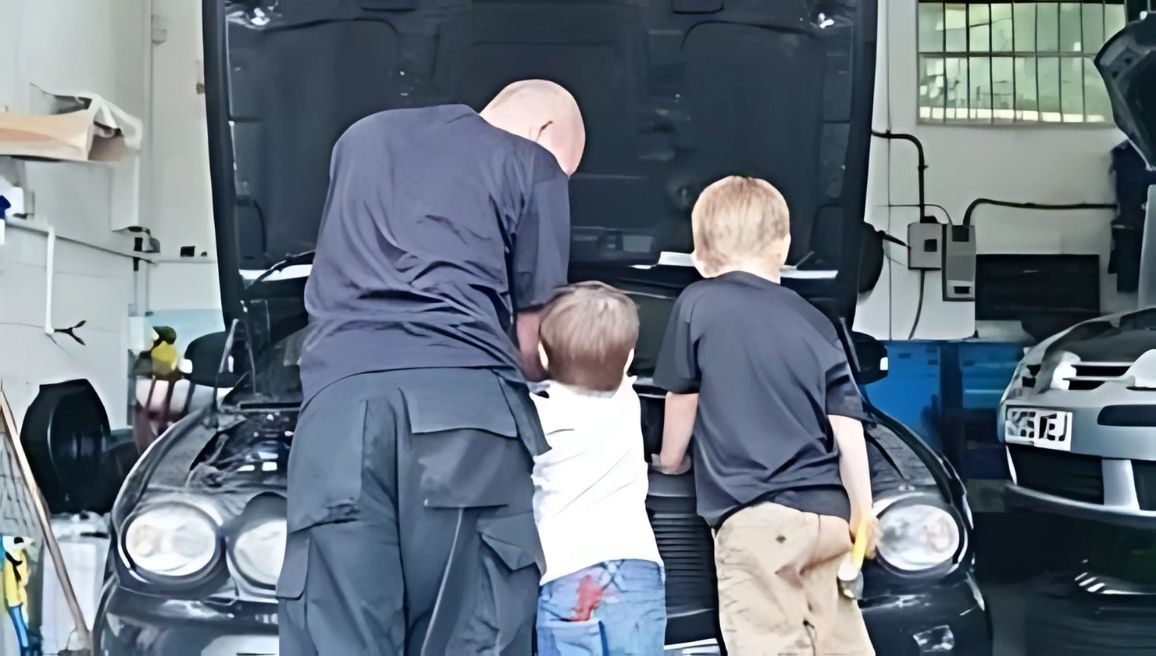 A man and two children are looking under the hood of a car.