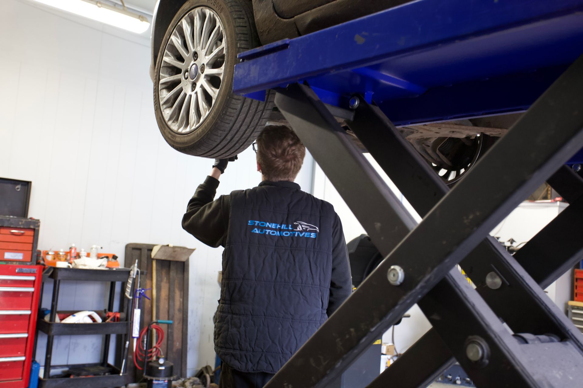 A man is working on a car on a lift in a garage.