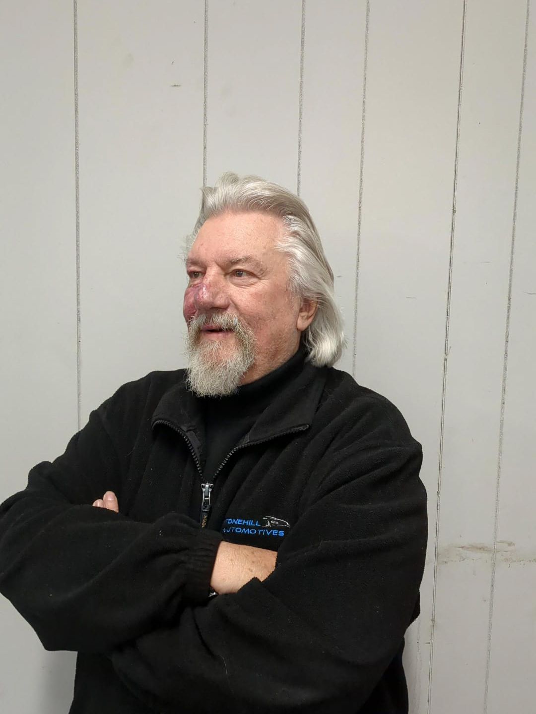 A man with a beard wearing a black jacket is standing with his arms crossed.