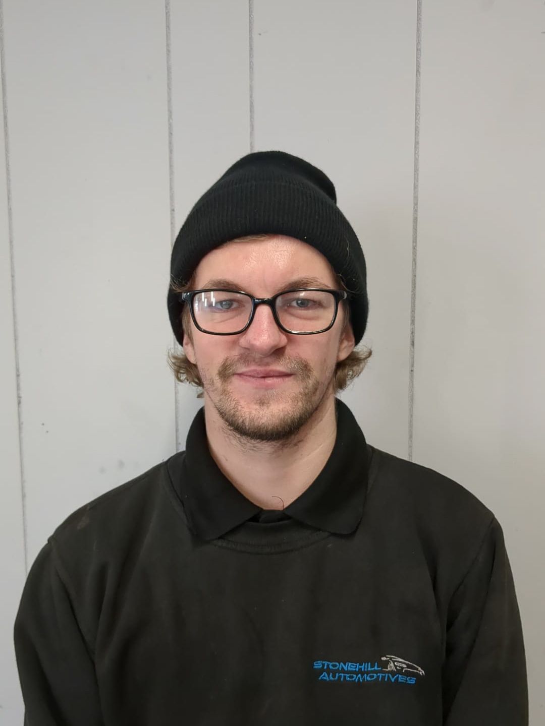 A man wearing glasses and a beanie is smiling for the camera.