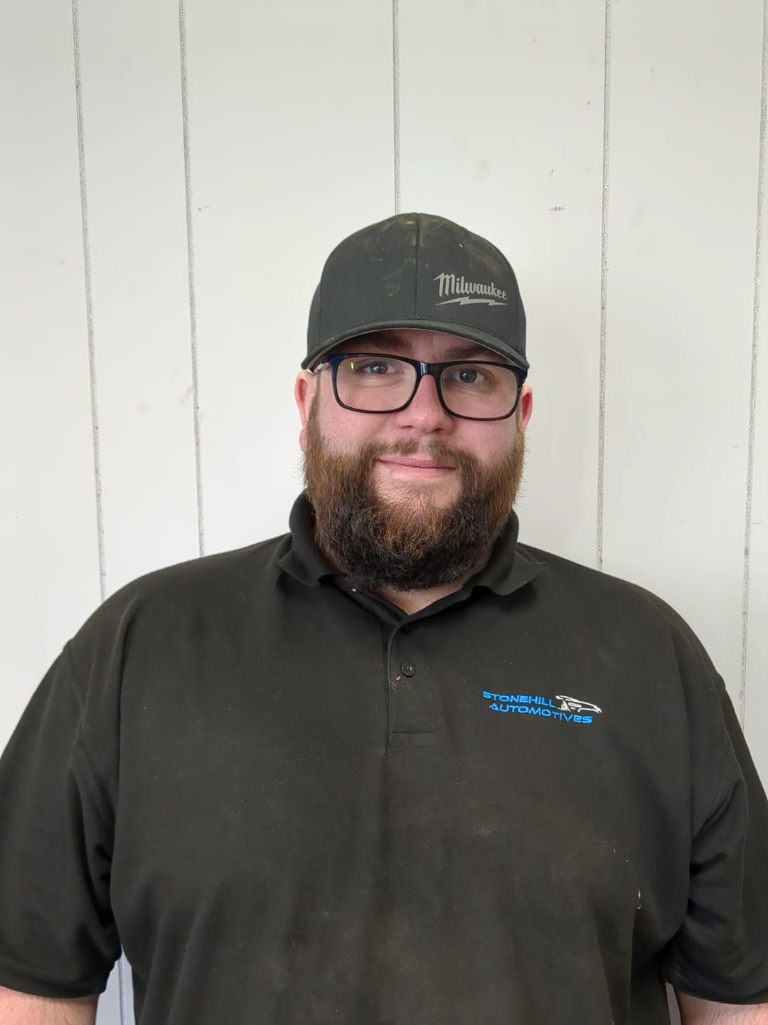 A man with a beard and glasses is wearing a hat and a black shirt.