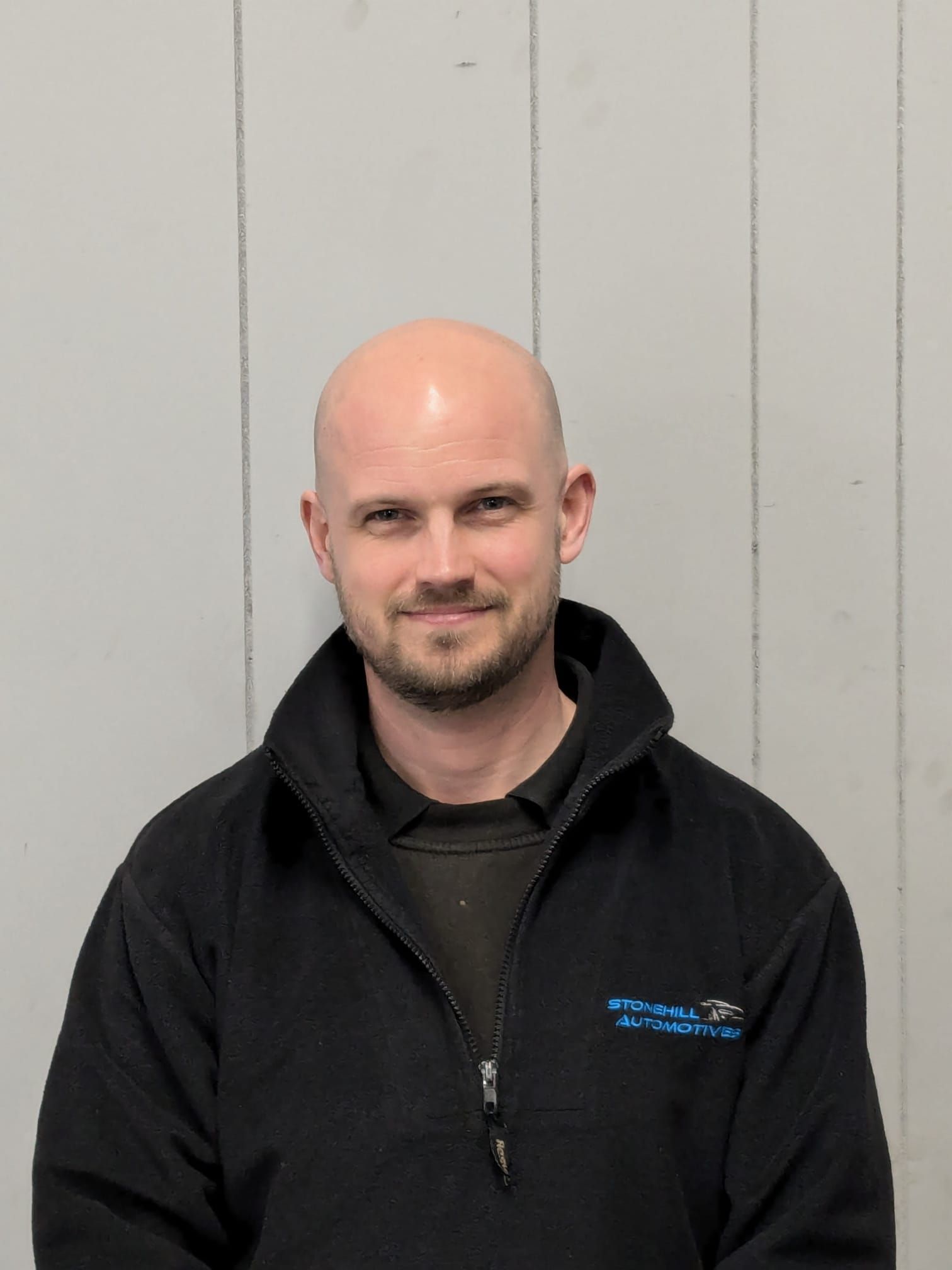 A bald man with a beard is wearing a black jacket.