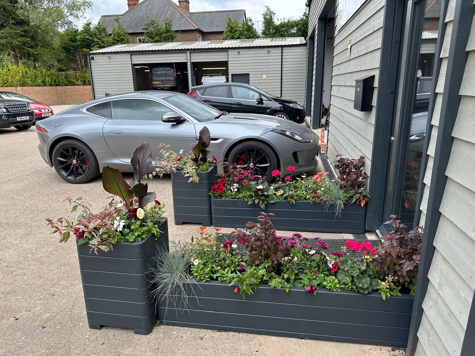 Two cars are parked in front of a building with planters filled with flowers.