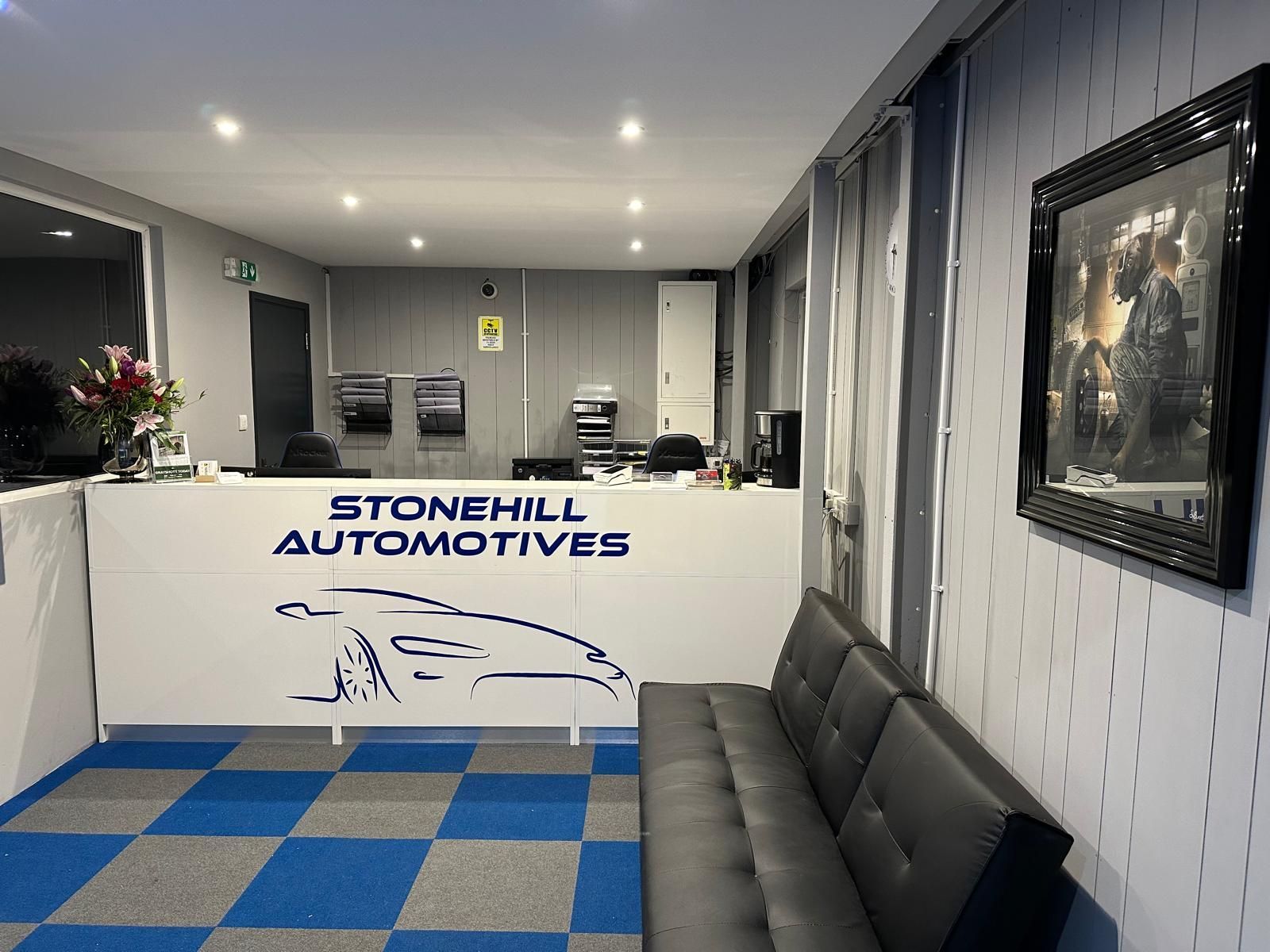 A waiting room with a couch and a counter for stonehill automotives.