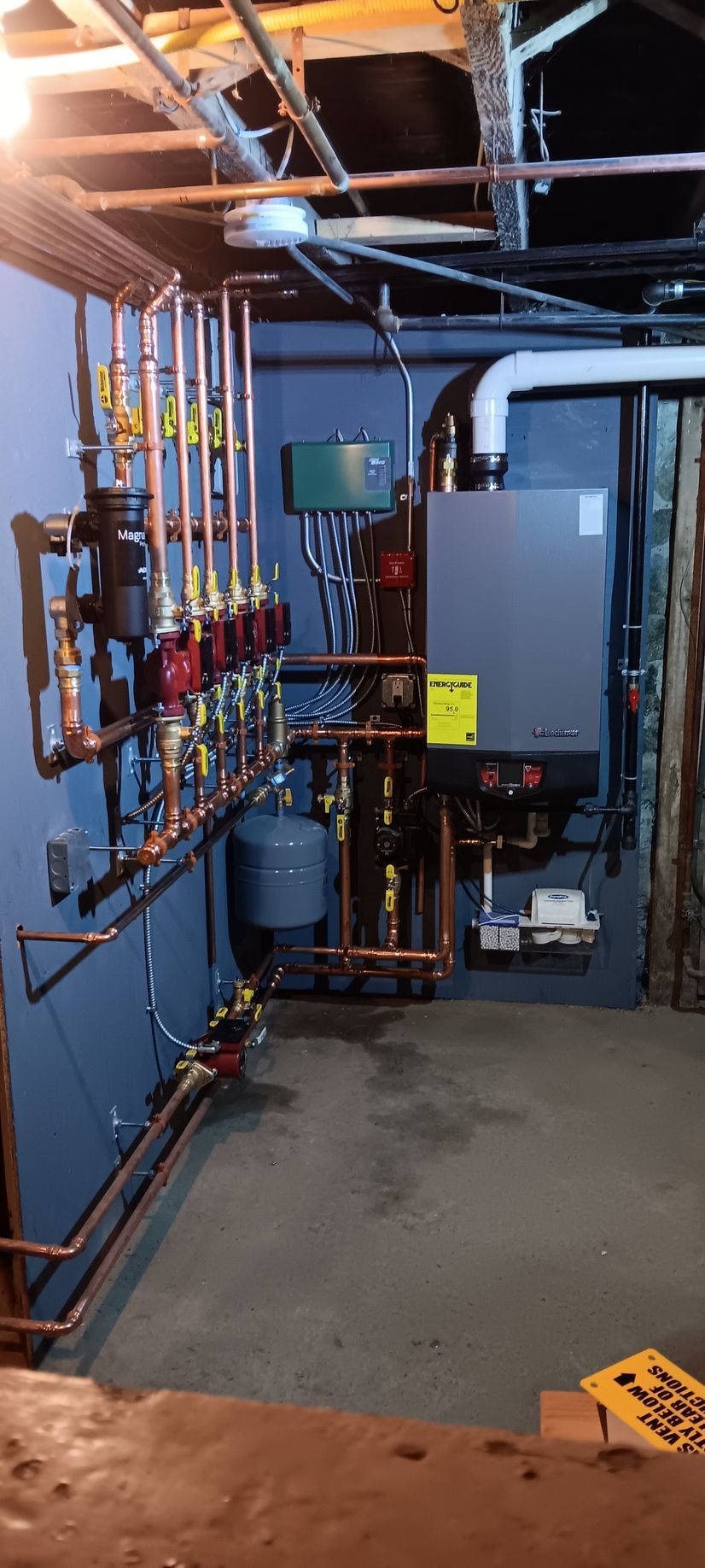 Plumbing system with copper pipes and red pumps on blue wall in a basement.