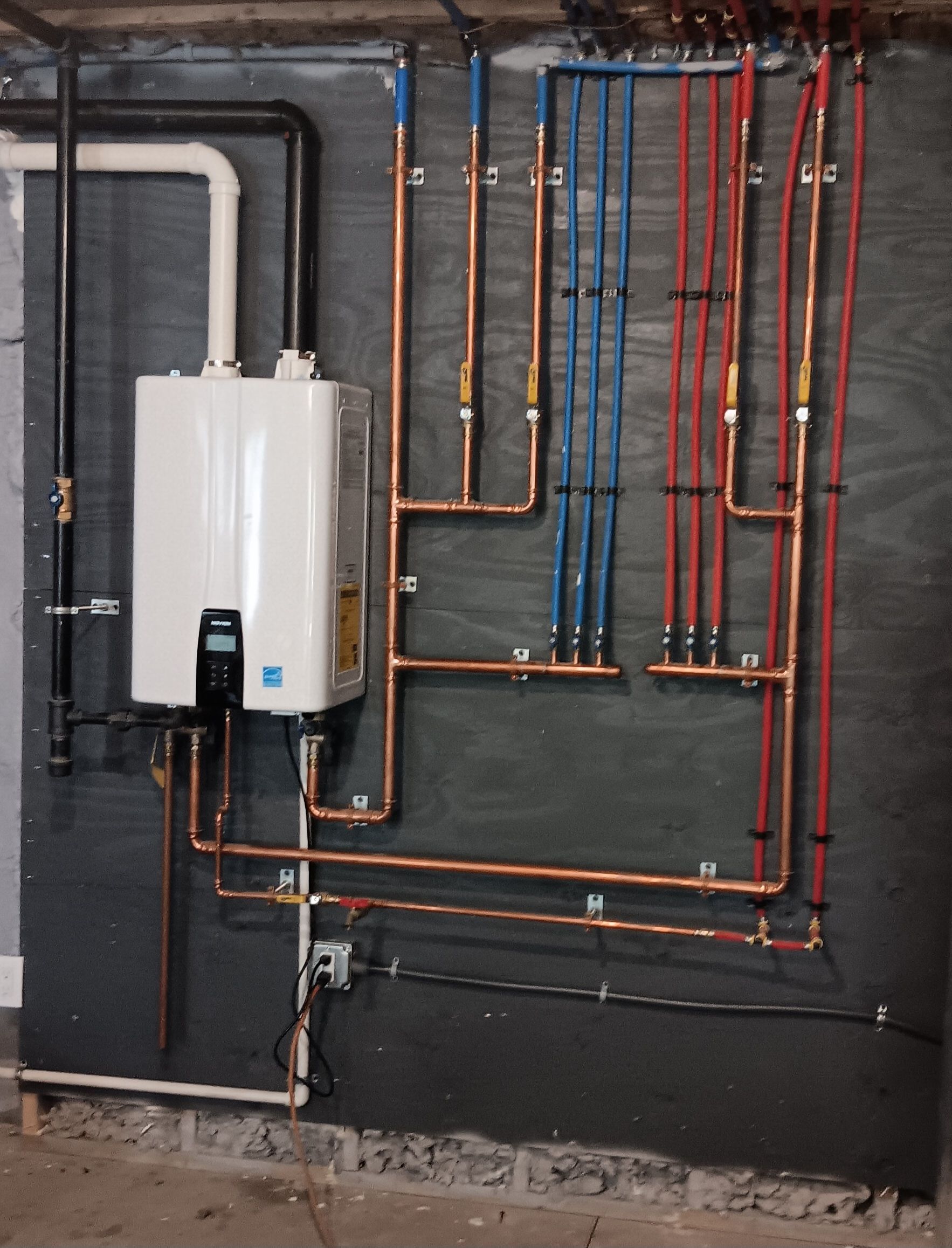 Copper plumbing and a water heater mounted on a black panel. Red and blue pipes are visible.