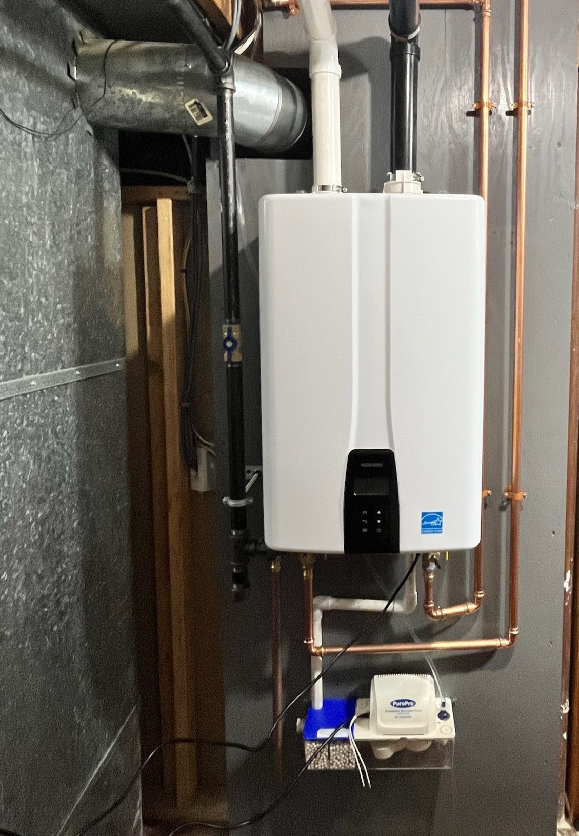 White tankless water heater mounted on a gray wall with copper pipes.