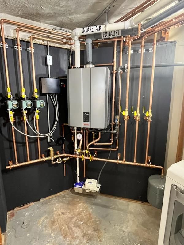 Copper pipes and a water heater installed on a black wall in a utility room.