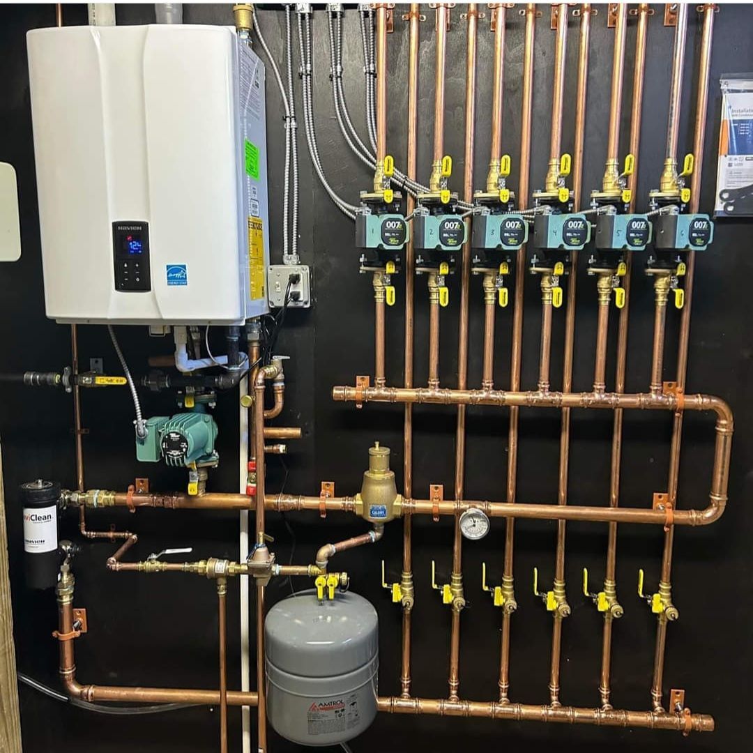 Copper piping and components for a hydronic heating system on a black wall, including a boiler and manifolds.