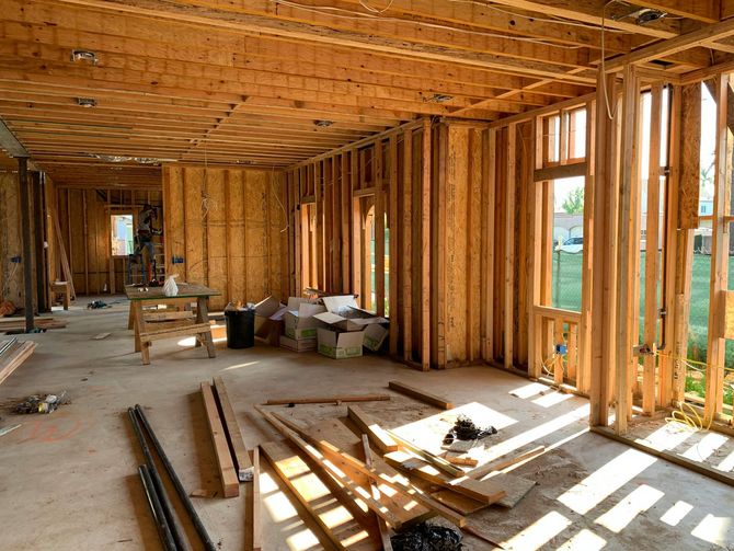 Interior view of a house under construction; wooden framing, sunlight streaming through window frames.