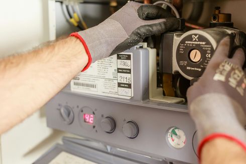 Person wearing gloves working on a boiler, checking a pump with a visible temperature gauge at 42.