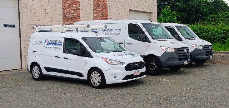 Three white service vans parked in front of a building. The first van has a roof rack, and all have company logos.