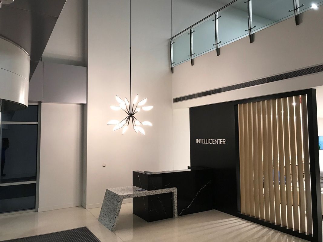 Modern office lobby with a black and white reception desk, decorative light fixture, and wooden slat divider.