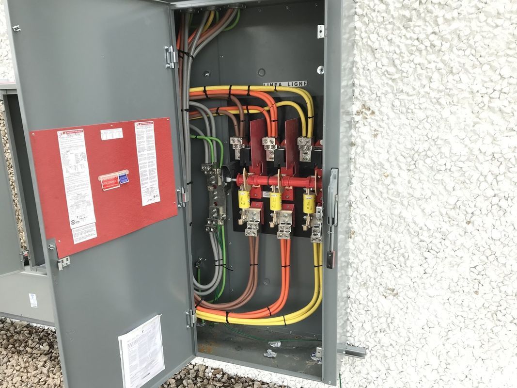 Electrical panel with colored wires and switches in a grey metal cabinet.