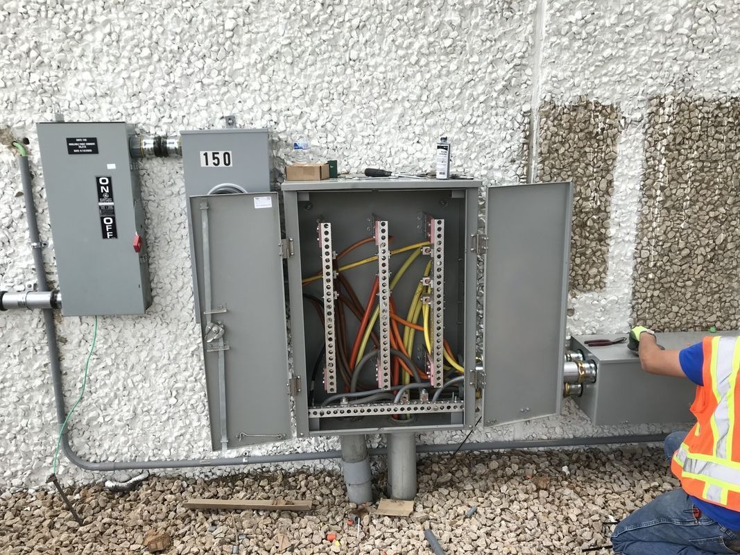 Exterior electrical panel with open door, wires, and a person in a safety vest.
