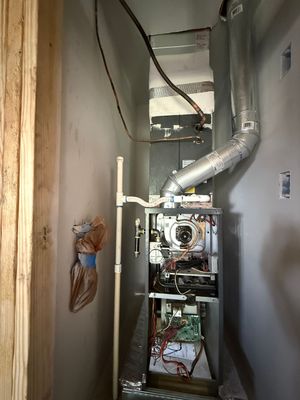 Narrow utility closet with exposed HVAC/furnace unit, vents, and pipes along the walls.