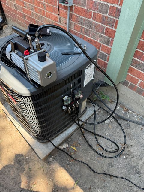 Outdoor air conditioner unit with a portable power supply on top, beside a brick wall and green post