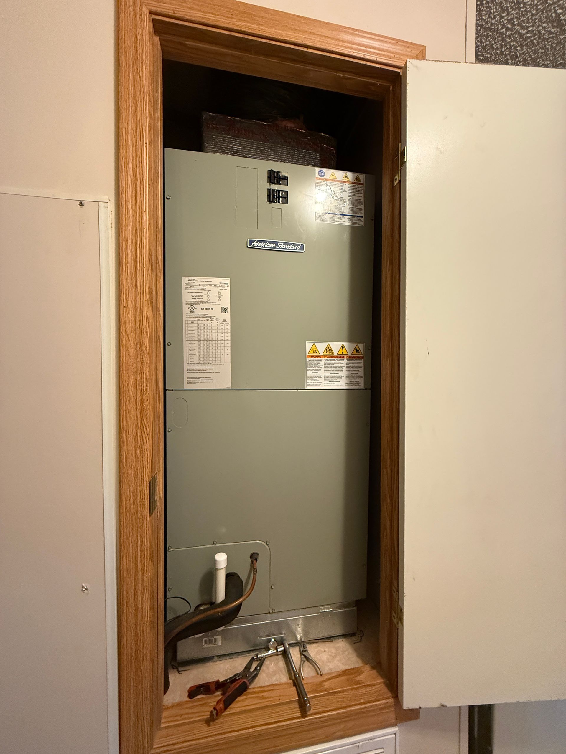 Open closet with a gray HVAC unit and exposed cables inside a wooden-framed wall opening
