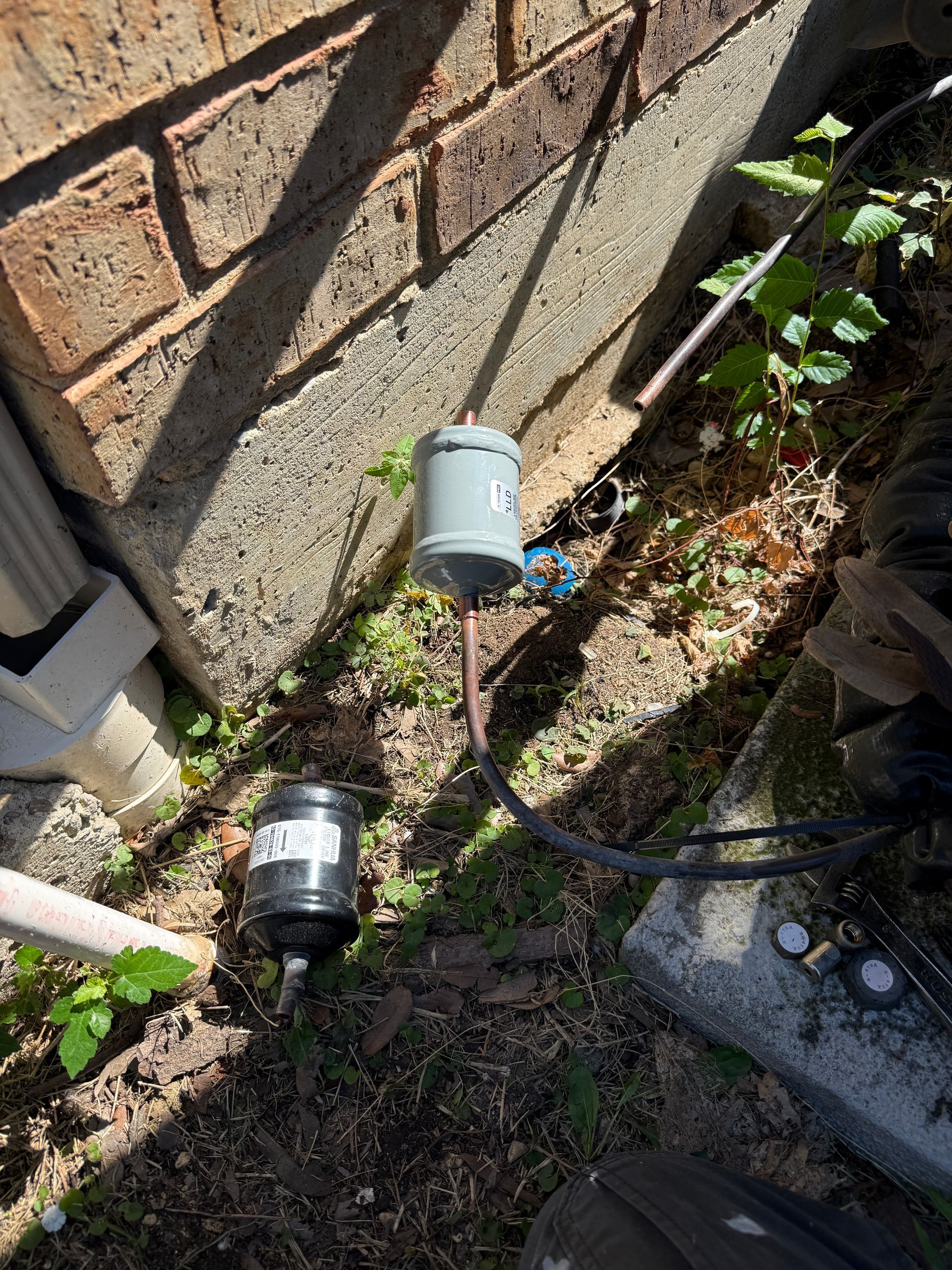 Two outdoor utility fixtures on a brick wall beside a garden bed, with cables and gravel below.
