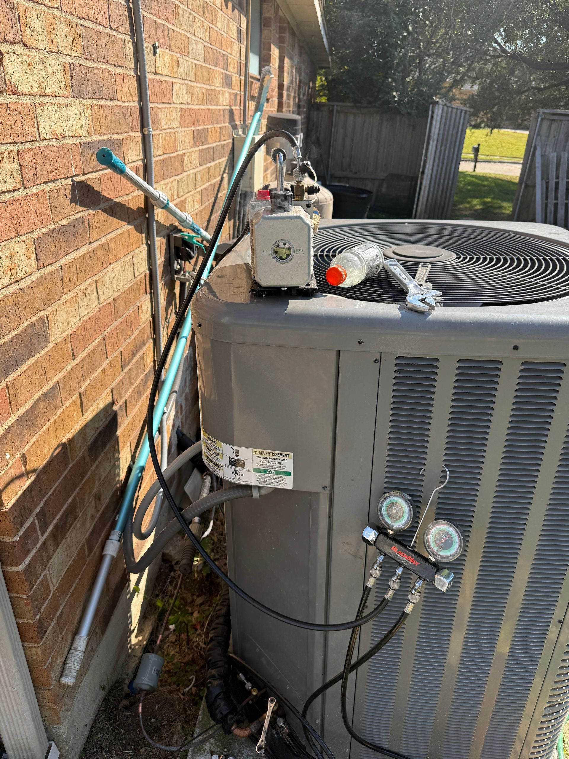 Outdoor air conditioner unit beside a brick wall with hoses and gauges attached
