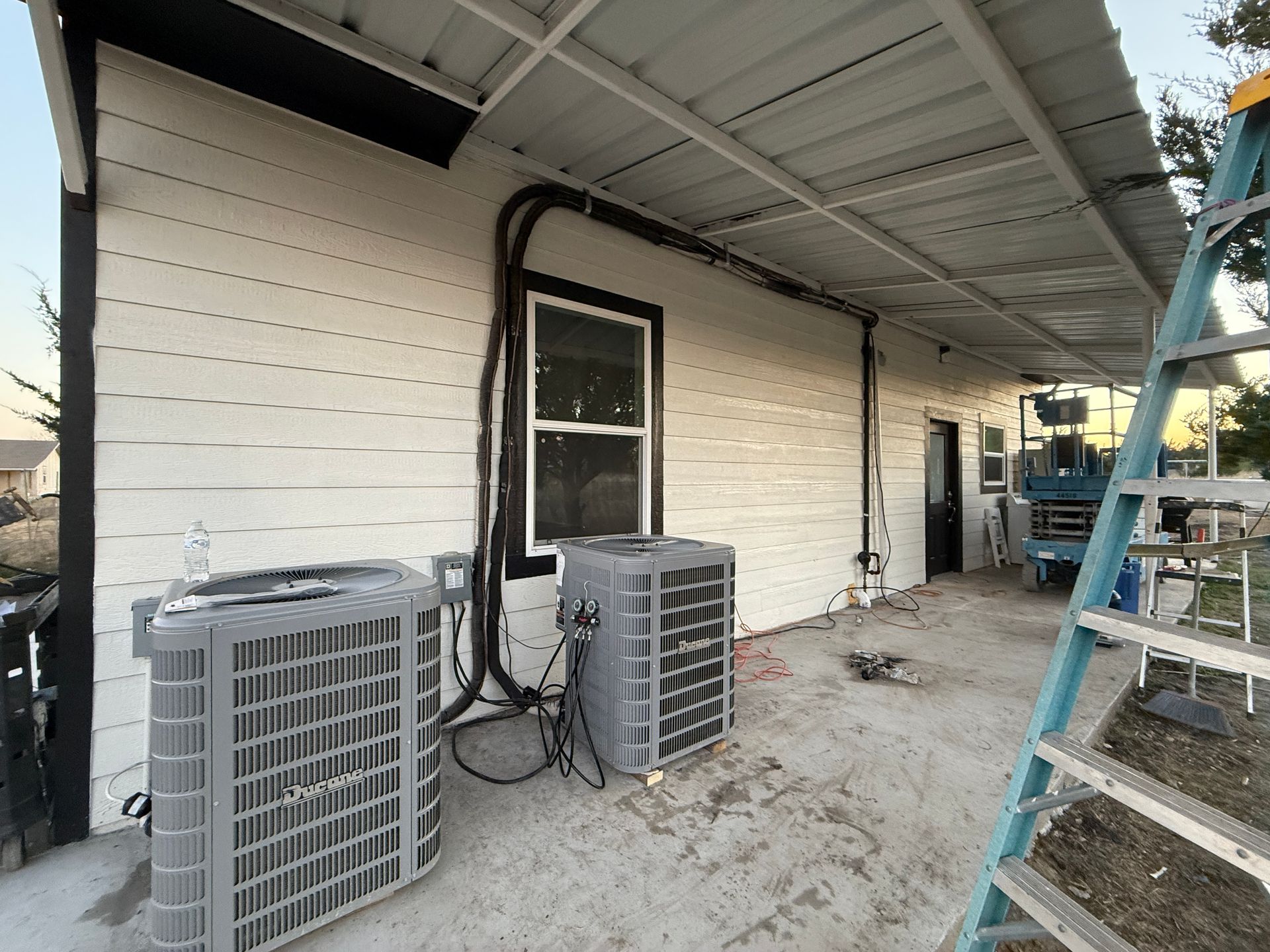 Exterior side of a building with two air conditioning units and a ladder under an overhang