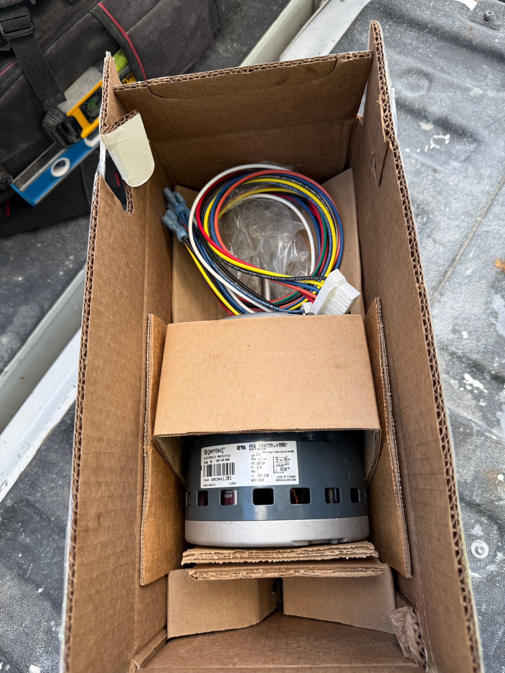 Cardboard box holding a small electric motor and bundled multicolored wires on a workbench.